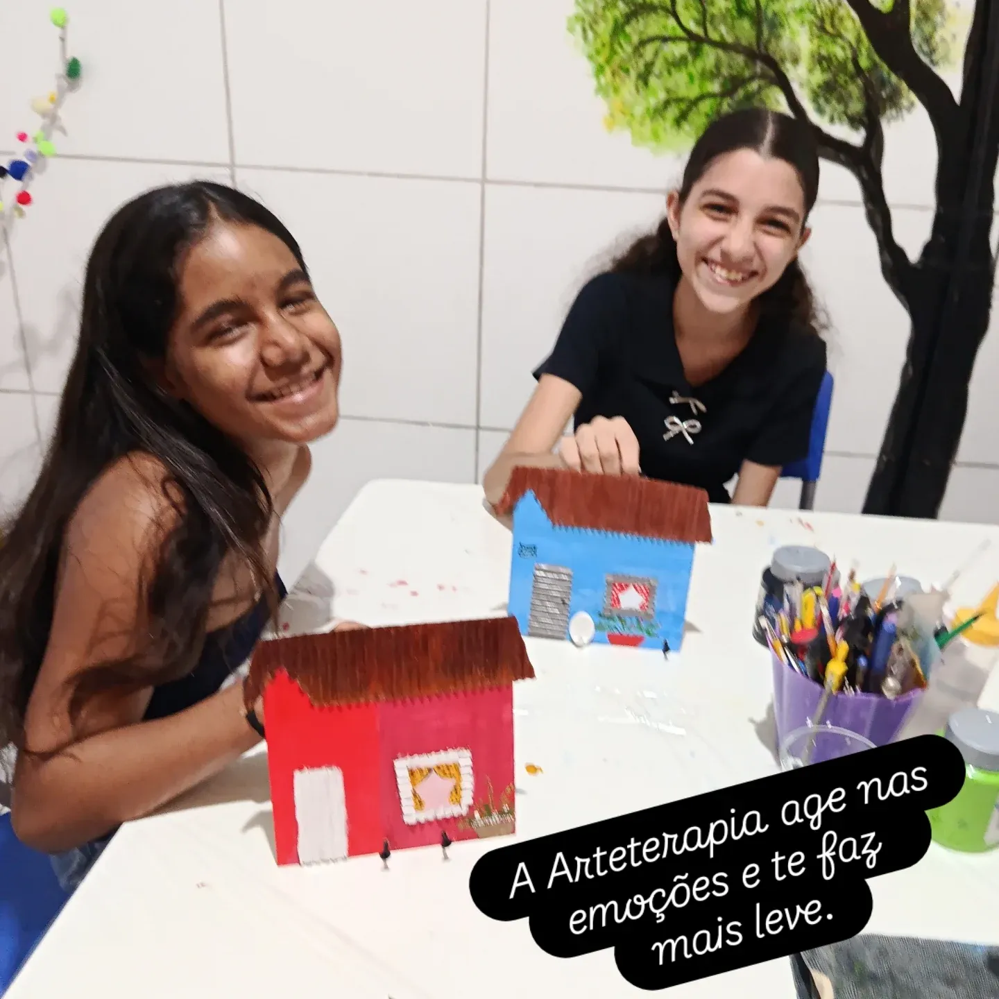 Duas meninas sorrindo ao lado das casinhas de madeira que pintaram.
