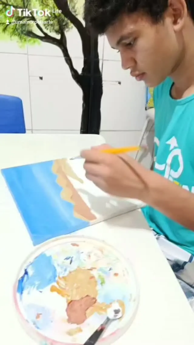 Adolescente pintando o mar azul numa tela.