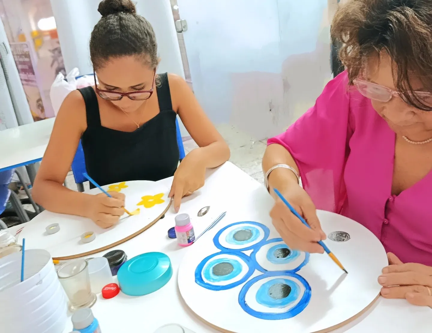 Duas mulheres pintando mandalas em círculos de madeira.