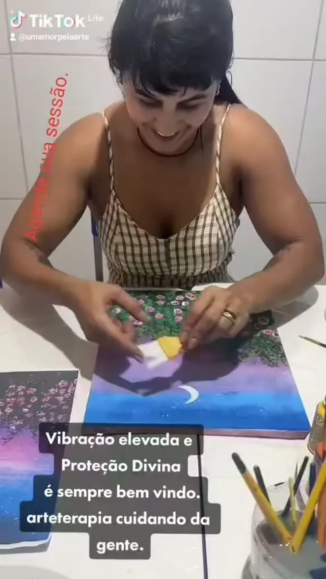 Aluna pintando uma tela de céu roxo com lua crescente.