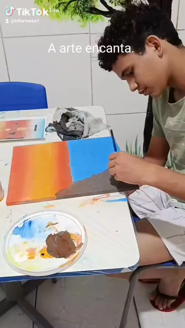 Adolescente pintando uma tela dividida entre o laranja do pôr do sol e o azul do céu.