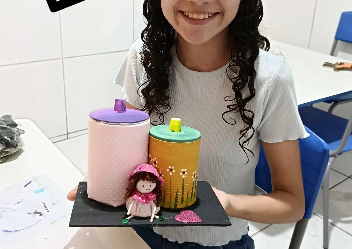 Porta-joias feitos com latas recicladas, pintados de rosa e amarelo, com uma bonequinha de pano.