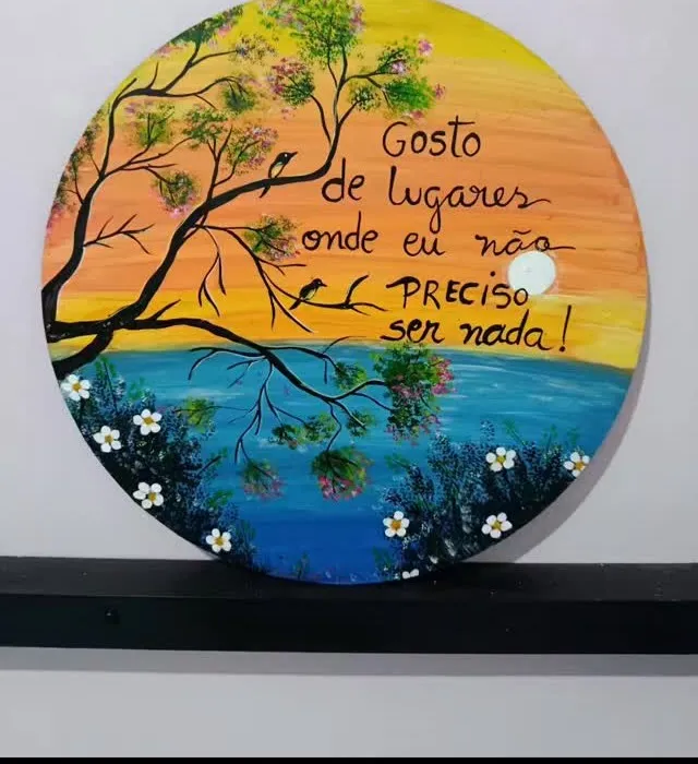 Relógio redondo de madeira pintado com mar, galho florido e a frase “Gosto de lugares onde eu não preciso ser nada”.