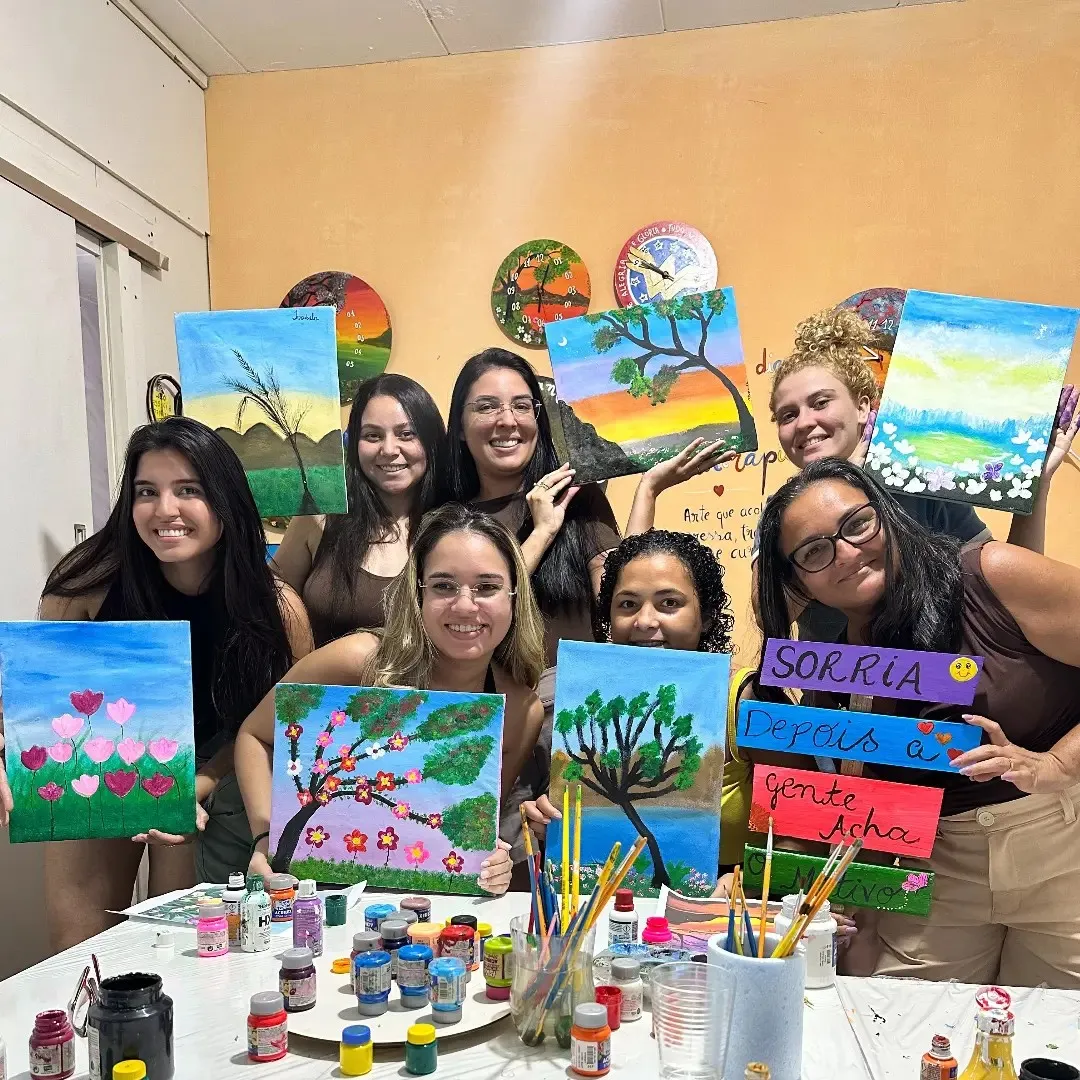 Grupo de mulheres sorrindo e mostrando as telas que pintaram juntas.