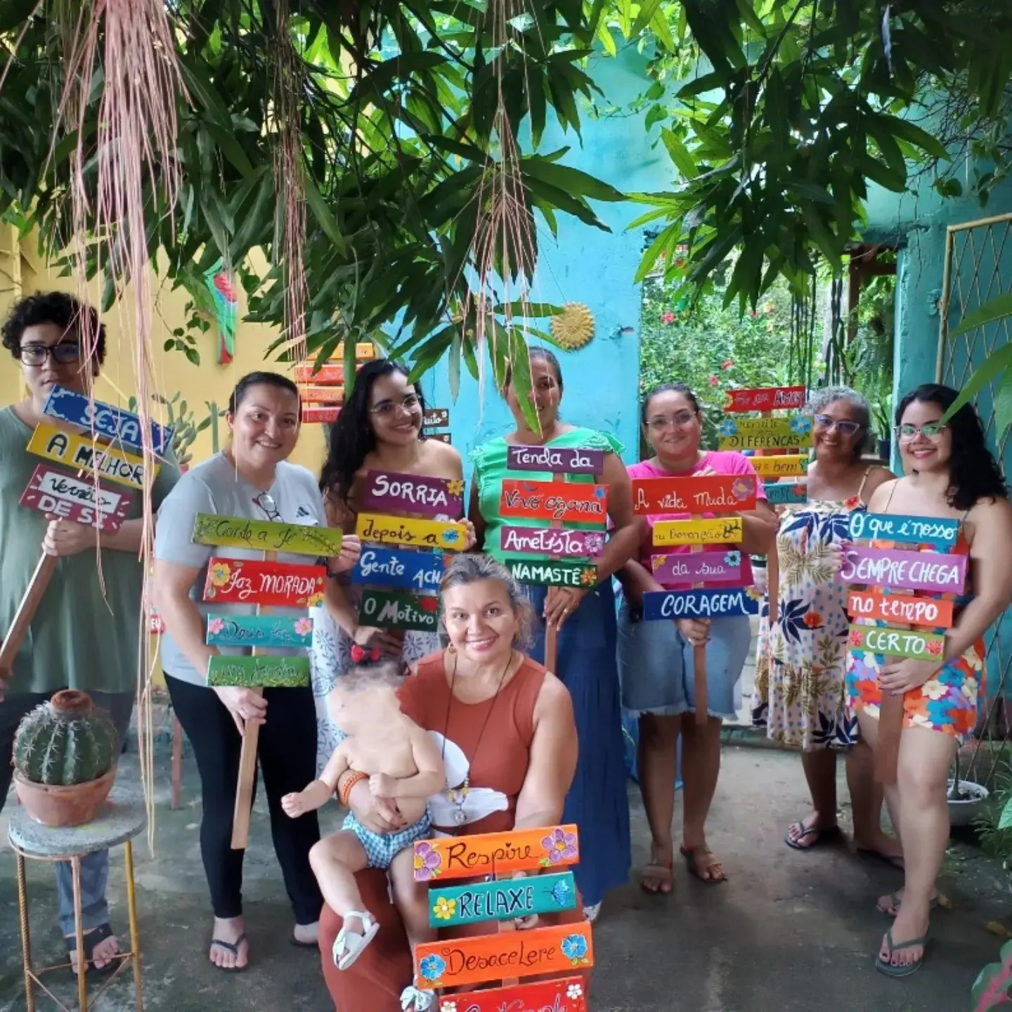 Grupo de alunas e alunos no quintal segurando plaquinhas de madeira pintadas com palavras como Sorria e Coragem.